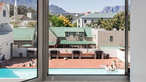 A view from a window of a residential area with a swimming pool, a church, and mountains in the background. - Spacious Central Apartment (Stellenbosch)