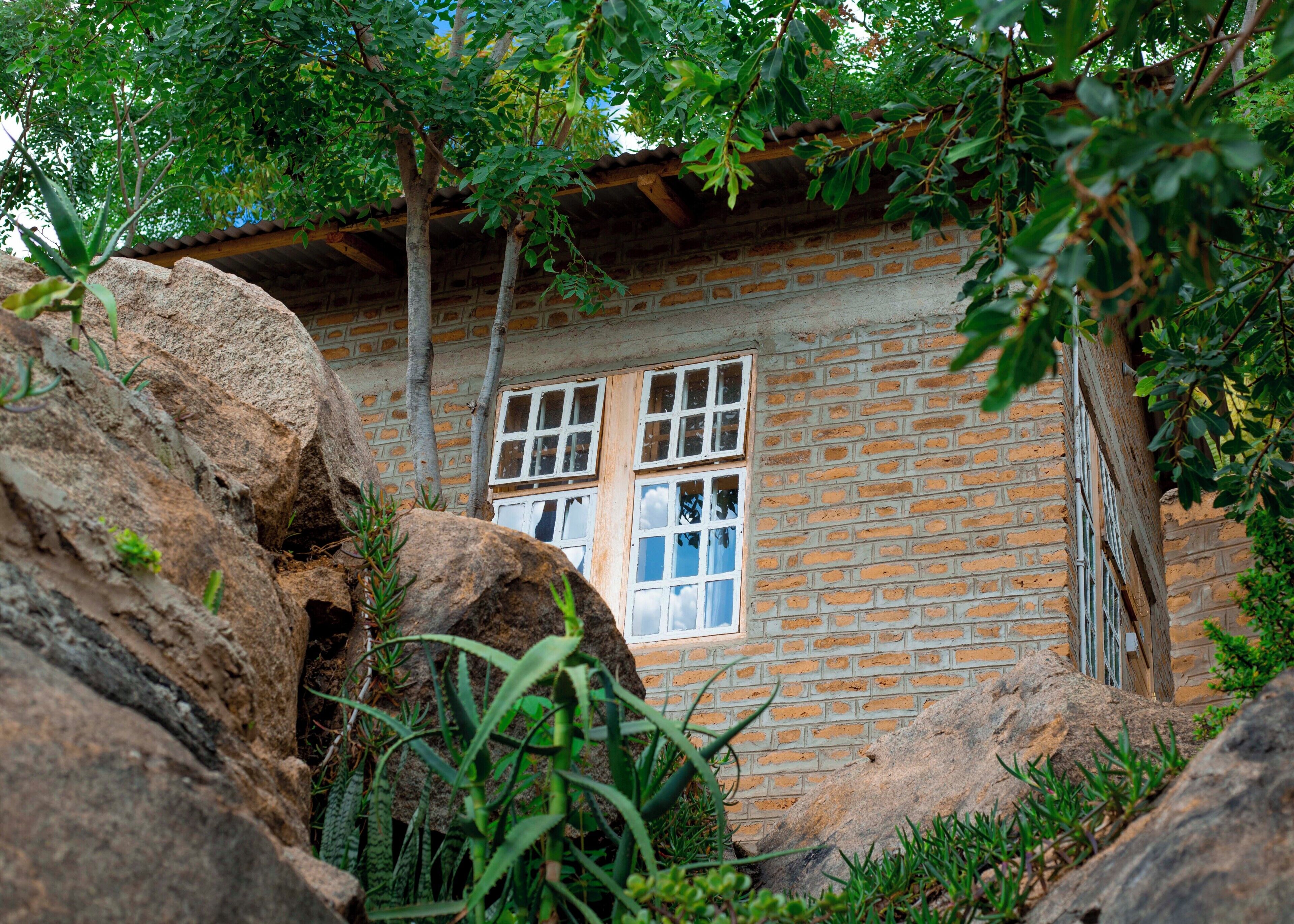 A rustic stone building with a window, surrounded by large rocks and greenery.