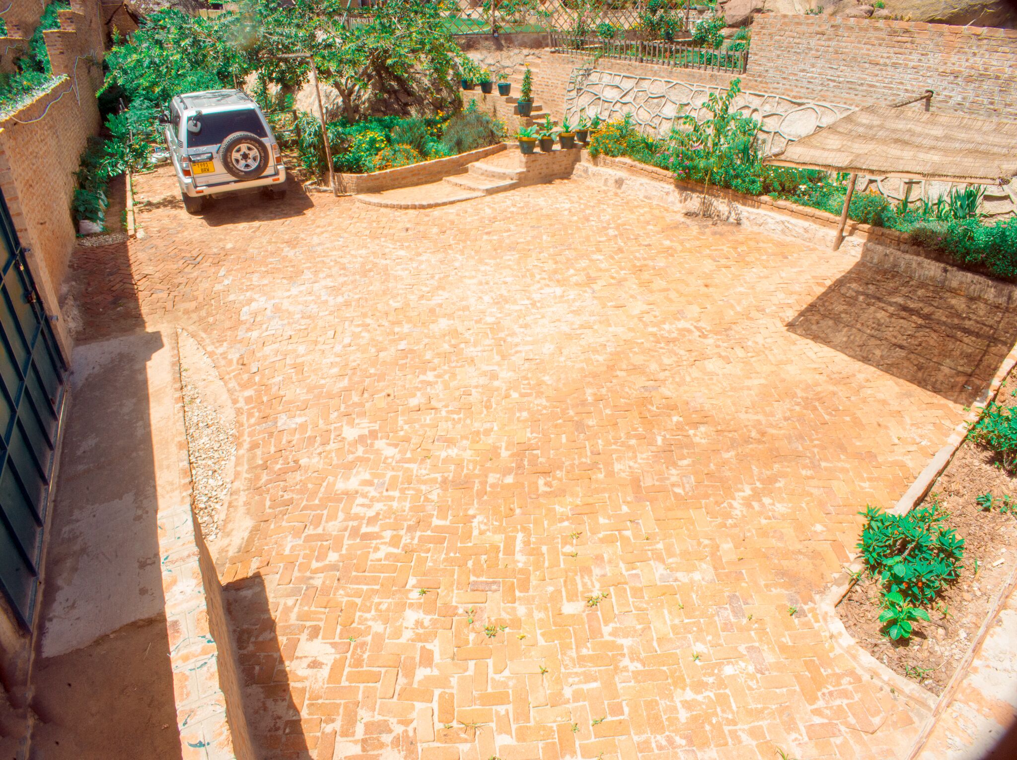 Une cour avec un sol pavé, un véhicule garé et de la verdure tout autour.
