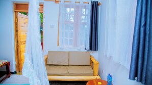 Una habitación con un sofá de madera, una mesita con una botella, una ventana con cortinas y una puerta que da al exterior.