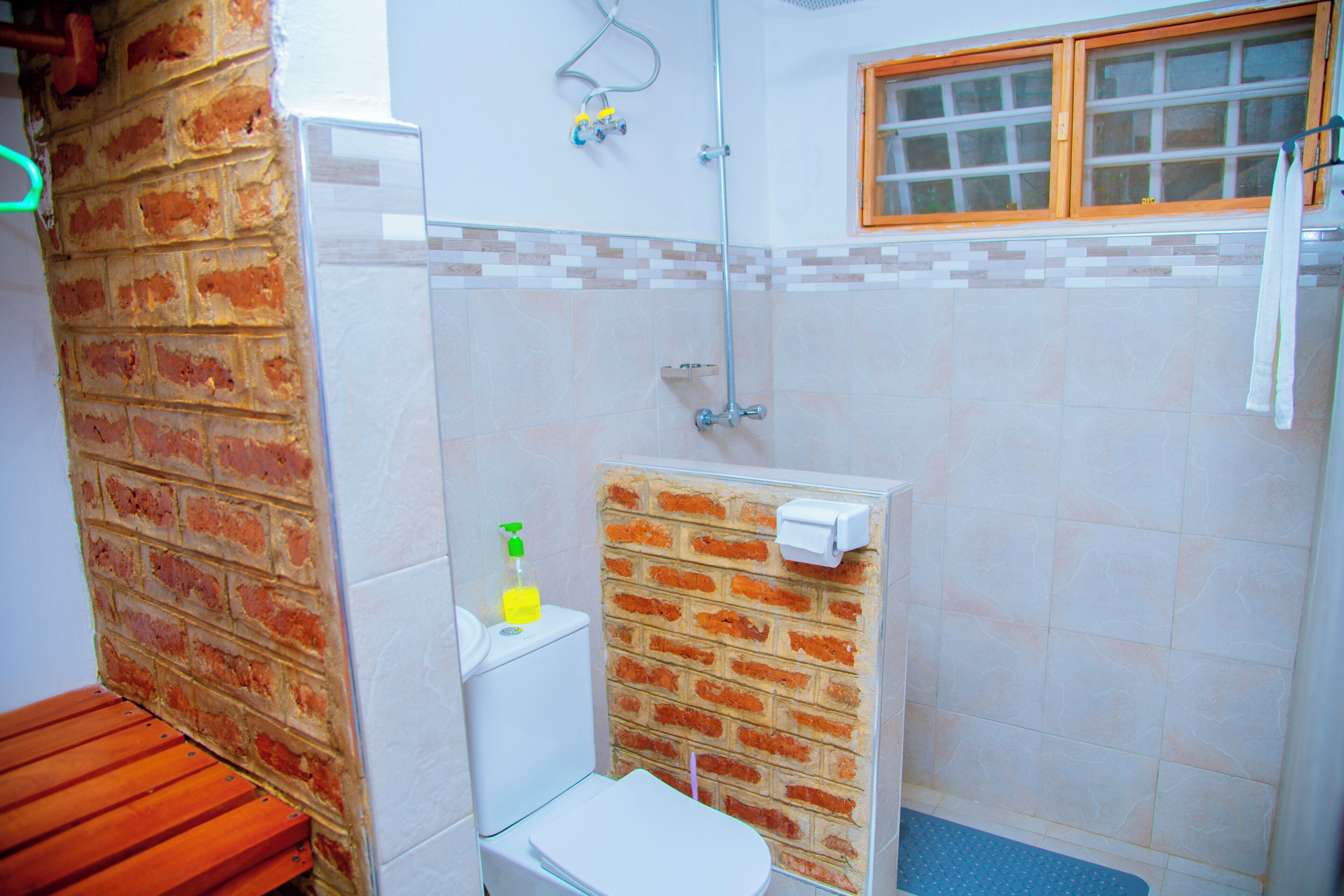Un baño con inodoro, ducha, ventana y pared de ladrillo.