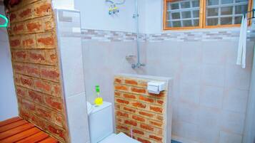 Un baño con inodoro, ducha, ventana y pared de ladrillo.
