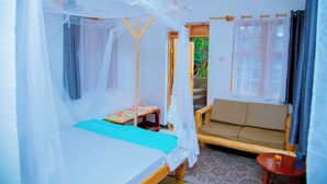 Una habitación con cama, sofá, una mesita y ventana con cortinas.