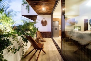 A modern interior with a dining area, wooden chairs, a sofa, and a kitchen with a refrigerator. - Nasha Tropical Bliss Plunge Pool Beach Club Access (Tulum)