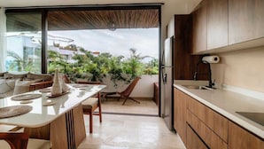 A modern kitchen with a large island, wooden cabinets, and a sliding glass door leading to a balcony with plants. - Nasha Tropical Bliss Plunge Pool Beach Club Access (Tulum)