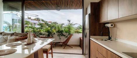A modern kitchen with a large island, wooden cabinets, and a sliding glass door leading to a balcony with plants.
