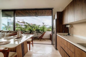 A modern kitchen with a large island, wooden cabinets, and a sliding glass door leading to a balcony with plants.