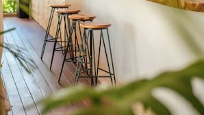 A bar area with wooden stools, woven pendant lights, and a wooden counter. - Nasha Tropical Bliss Plunge Pool Beach Club Access (Tulum)