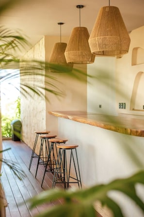 A bar area with wooden stools, woven pendant lights, and a wooden counter.