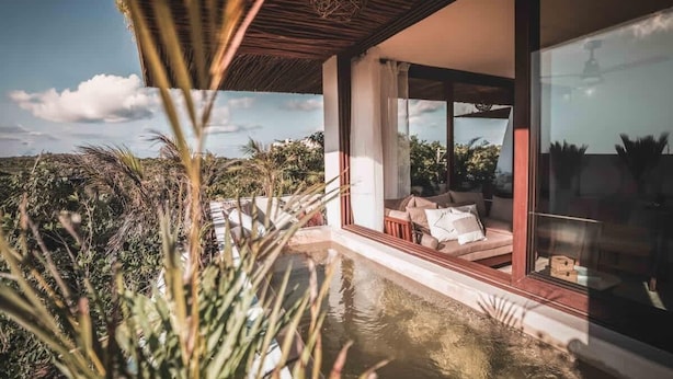 A modern house with a glass door leading to a balcony with a pool, surrounded by vegetation. - Nasha Tropical Bliss Plunge Pool Beach Club Access (Tulum)