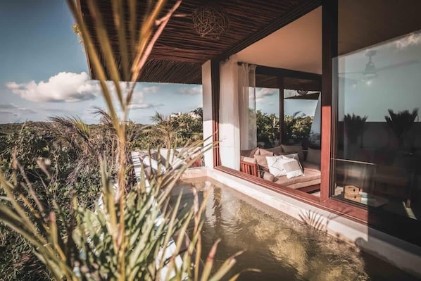 A modern house with a glass door leading to a balcony with a pool, surrounded by vegetation.