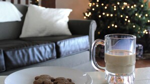 Ein Weihnachtsbaum mit Lichtern, eine Glühwein-Tasse und Lebkuchen auf einem Tisch.