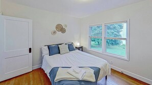 Ein Schlafzimmer mit Bett, Nachttisch, Fenster mit Jalousien und einer Tür.