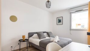 Ein modernes Schlafzimmer mit Bett, Nachttisch, Lampe und Blick ins Freie.