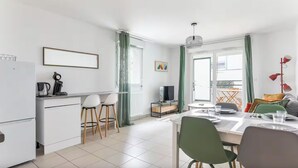 Eine moderne Küche mit Kühlschrank, Kaffeemaschine und Barhocker. Ein Esstisch mit Stühlen und ein Fernseher auf einem Lowboard.