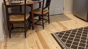 Ein Essbereich mit einem Holztisch und Stühlen, einem gerahmten Bild an der Wand, einer Tür mit Fenster und einem Kühlschrank.