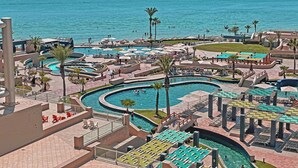 Een resort met meerdere zwembaden, palmbomen en uitzicht op de oceaan.