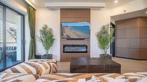Een moderne woonkamer met een grote flatscreen-tv, bevestigd aan een houten wandpaneel, met aan weerszijden twee potplanten.