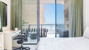 Een hotelkamer met een bed, bureau, stoel en uitzicht op het strand.