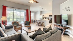 A modern living room with a sofa, chairs, a coffee table, a TV, and a kitchen area in the background. - -NEW LISTING- Disney home w/ Pool, Hot Tub & 2 King En-Suites- 4 miles to Disney (Kissimmee)