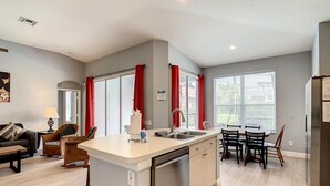A modern kitchen with a central island, a dining area with chairs, and a living room with a sofa and a lamp. - -NEW LISTING- Disney home w/ Pool, Hot Tub & 2 King En-Suites- 4 miles to Disney (Kissimmee)