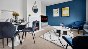 Een moderne woonkamer met een open haard, een eethoek en een zithoek met blauwe stoelen.