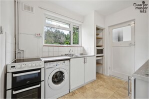 A compact kitchen with a built-in oven, washing machine, and a window above the sink.