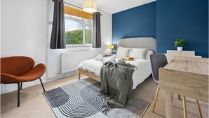 Een moderne slaapkamer met een bed, een stoel, een bureau en een raam met gordijnen.