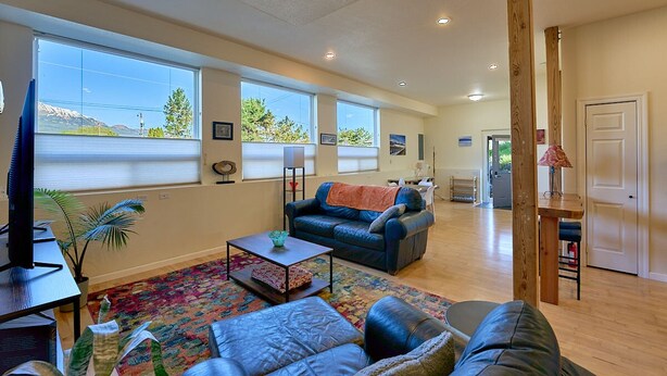 A spacious living room with large windows, a sofa, a coffee table, and a television. - Blue Moon Retreat ~~ Spacious duplex unit with SAUNA and a stunning view (Joseph)