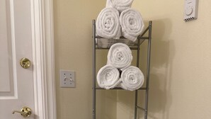 A metal shelf unit with towels and a basket in a corner of a room with a white door and beige walls. - Blue Moon Retreat ~~ Spacious duplex unit with SAUNA and a stunning view (Joseph)
