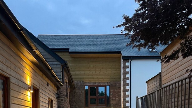 A pathway leading to a building with a stone facade and wooden siding, illuminated by ground lights.