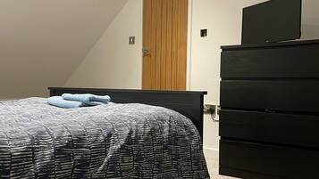 Ein Schlafzimmer mit einem Bett, einer Kommode, einem Fernseher auf der Kommode und einer Holztür.