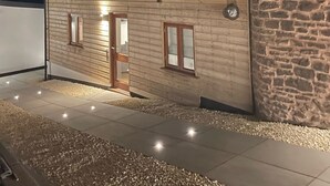 A modern building with a wooden facade and stone wall, featuring a door and windows, illuminated by exterior lighting.