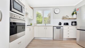 A modern kitchen with white cabinetry, a stainless steel dishwasher, a microwave, and a coffee machine. - The Palms Retreat - Top Floor Apartment style (Nelson Bay)