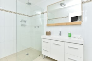 Een moderne badkamer met een douchecabine van glas, witte kastjes en een spiegel boven de wastafel.