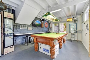 Een biljartkamer met een pooltafel, een dartbord en een ingelijst foto van een stadion.