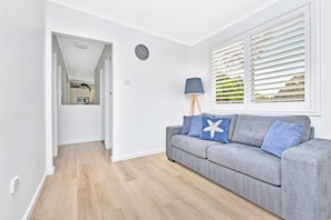 A modern living room with a grey sofa, a starfish pillow, a floor lamp, and a view through white shutters.