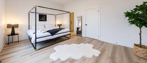 Un dormitorio con cama con dosel, alfombra mullida blanca, lámpara de noche y planta en maceta.