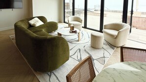 Un amplio salón con un gran ventanal, un sofá verde, un sillón blanco y una mesa de centro de mármol.
