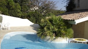 En swimmingpool med krystalklart vand, omgivet af en hvid mur og et tag med fliser.