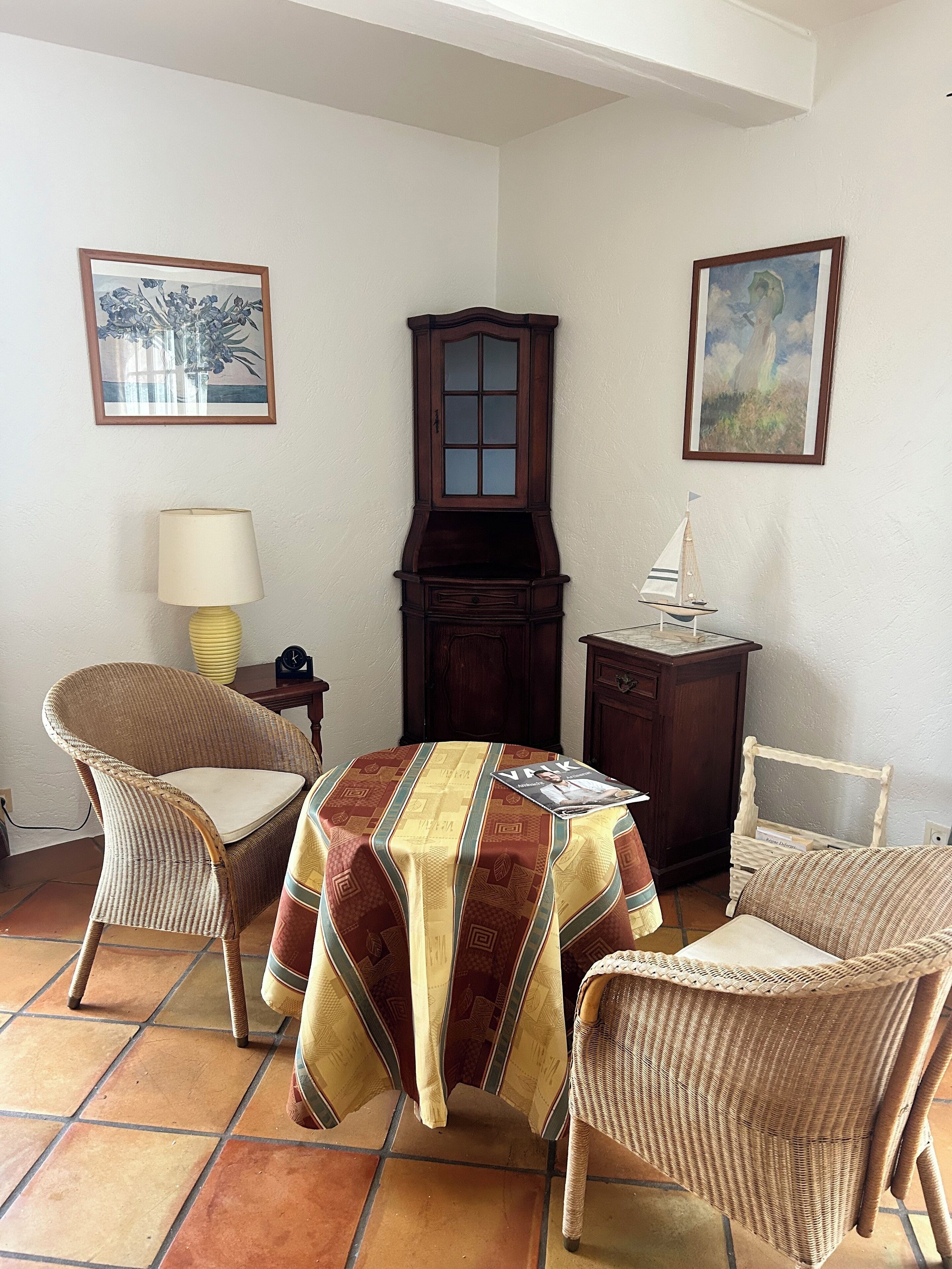Ein Zimmer mit Esstisch, zwei Korbstühlen, einem Schrank und zwei gerahmten Bildern an der Wand.