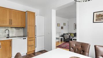 Ett modernt kök med träskåp, ett vitt kylskåp och en matplats med ett vitt bord och bruna stolar.