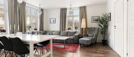 A modern living room with a dining area, large windows, and a red rug.