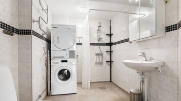 A modern bathroom with a washing machine, a shower, and a sink.