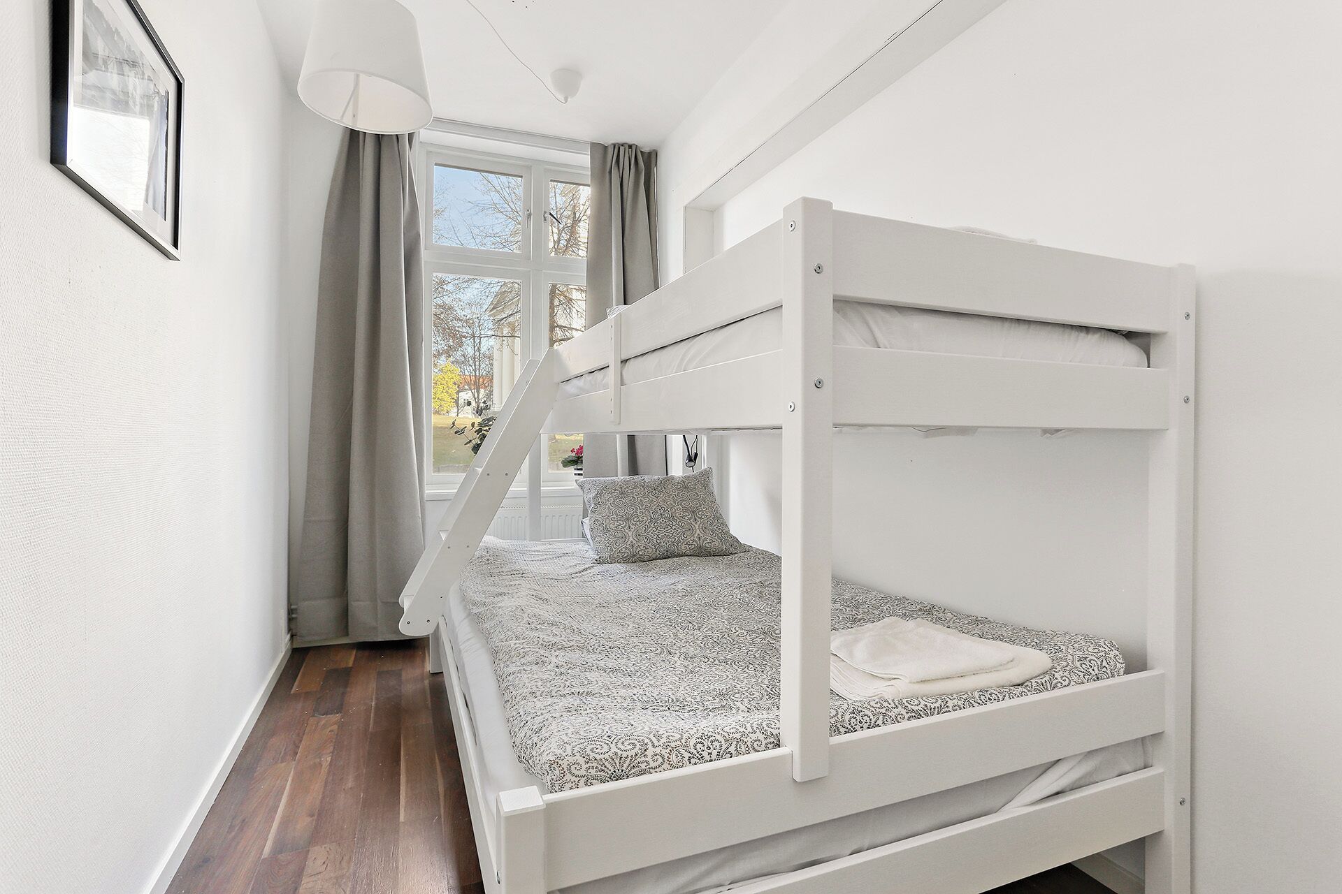 A bunk bed room with a window, curtains, and a hanging light fixture.