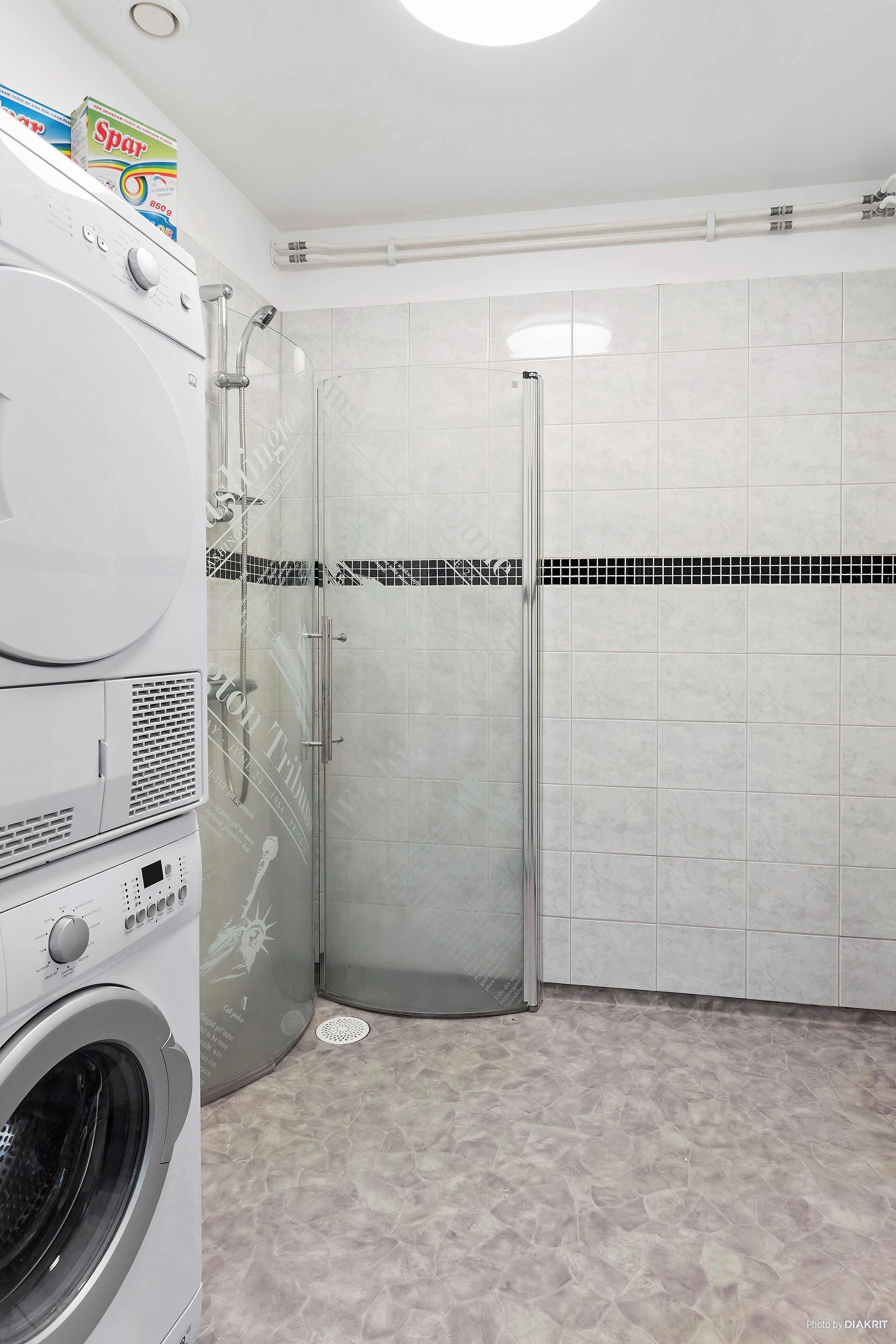 A modern bathroom with a washing machine, a glass shower enclosure, and a tiled floor.