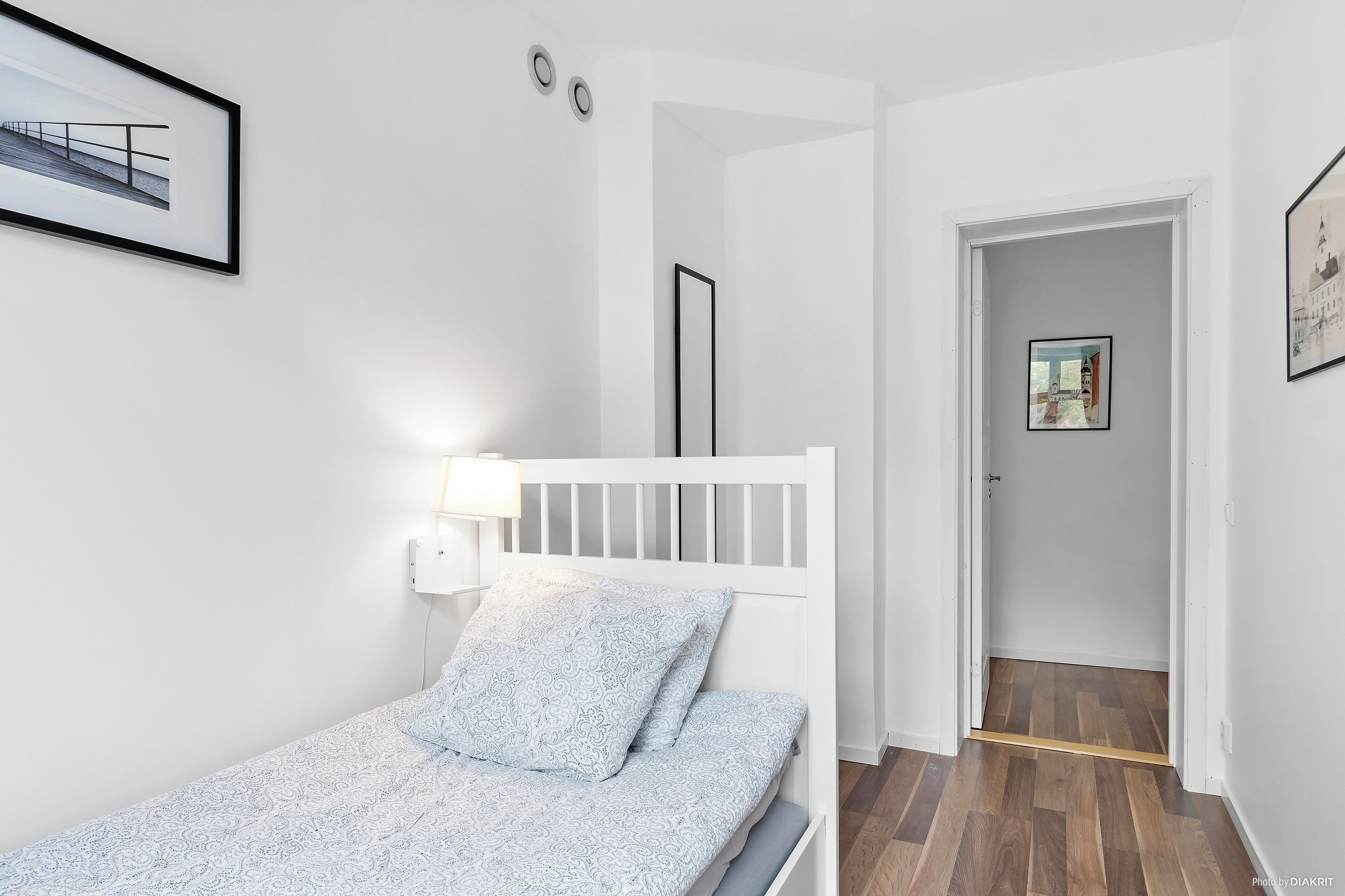 A bedroom with a white bed, patterned bedding, a bedside lamp, and a framed picture on the wall.