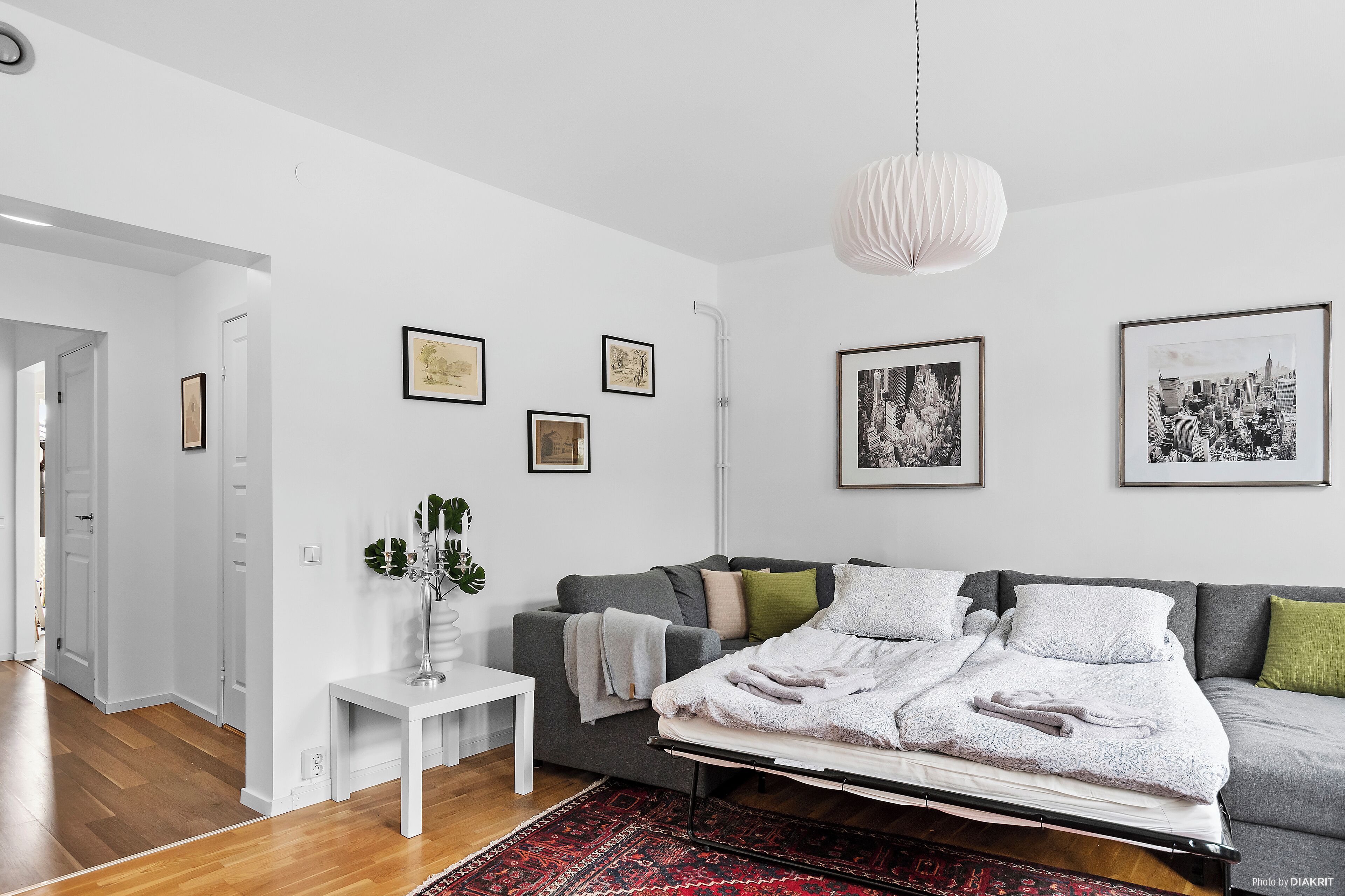 Ett modernt sovrum med en säng, en grå soffa, ett vitt sängbord och en röd, mönstrad matta.