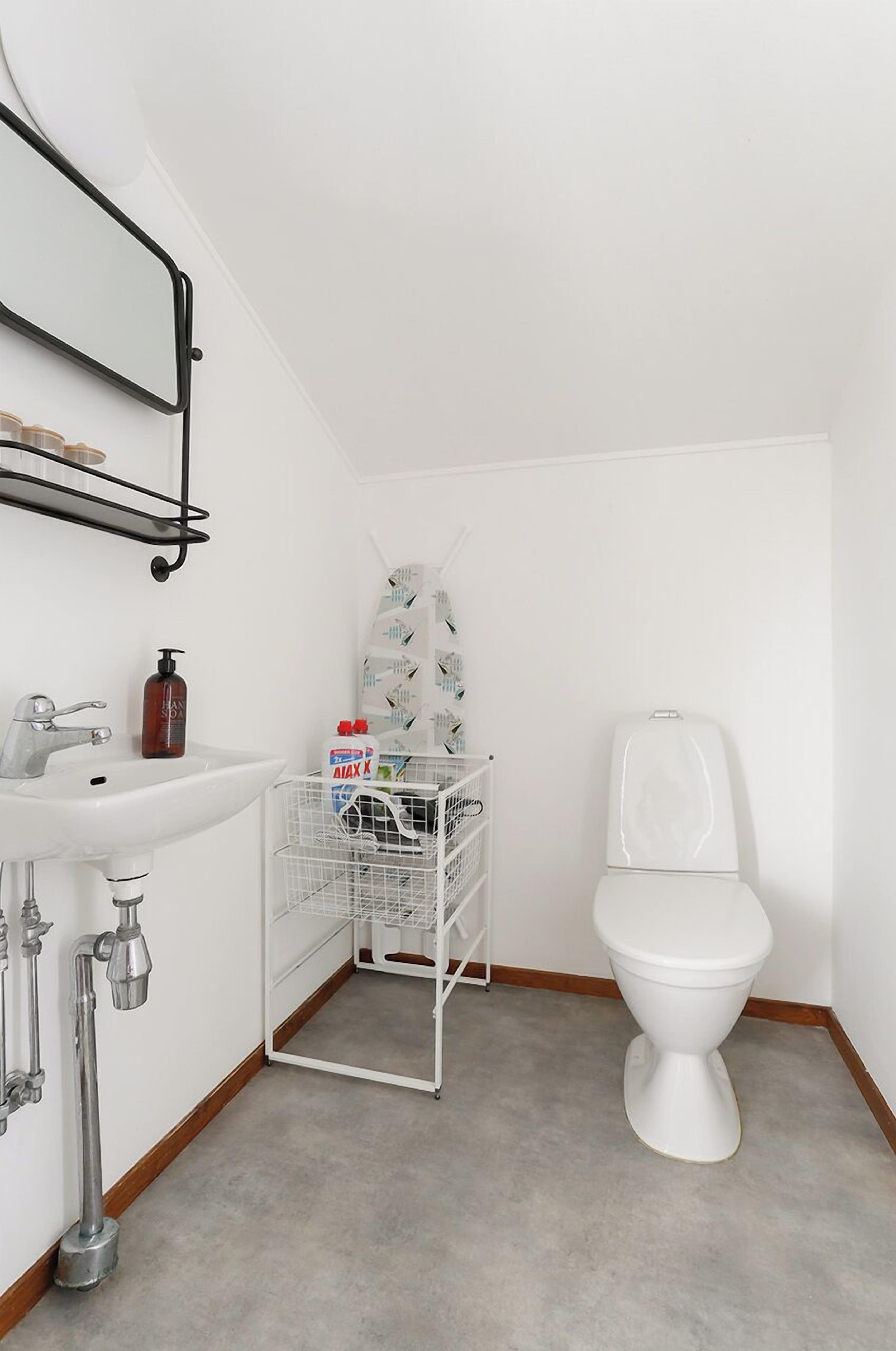 Ett litet, rent badrum med en vit handfat, en toalett och en metallhylla ovanför handfatet.