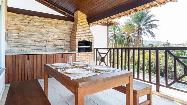An outdoor patio with a stone wall, a brick oven, and a table set for dining. - Bz73 Geribá! Casa c/ piscina privativa 5 Suítes! (Búzios)